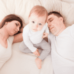 baby looking up with one parent on each side asleep