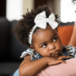 Toddler with large white bow tie on head looking up at mother