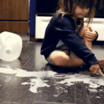 Toddler girl sitting around spilled gallon of milk on the floor