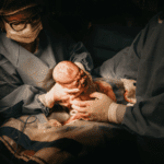 two doctors in scrubs holding a newborn baby